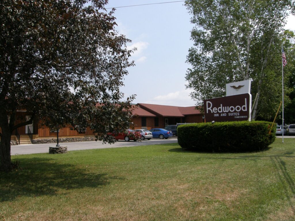 A brown building with cars parked outside and a sign reading Redwood Inn and Suites on a green lawn.