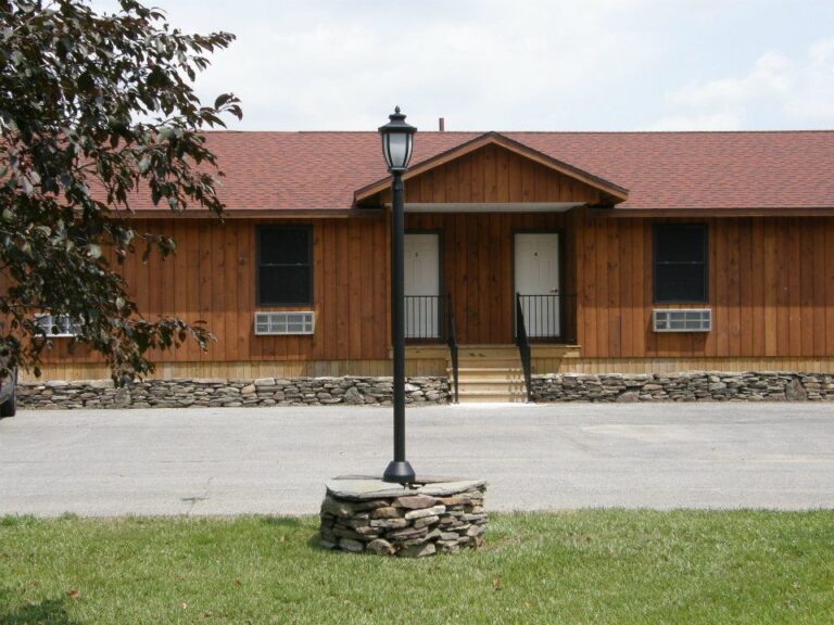 Wooden building with stone foundation, two white doors, black lamp post in front, and grass in the foreground.