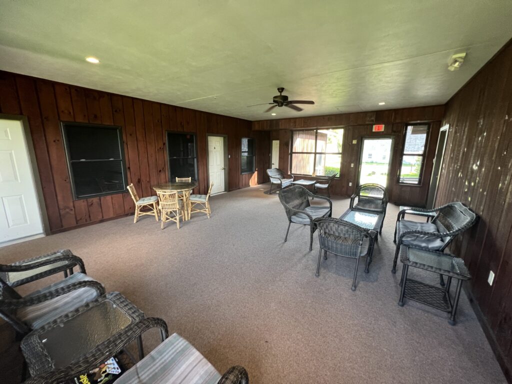 A sunroom with wooden walls, wicker furniture, a ceiling fan, and windows letting in natural light.